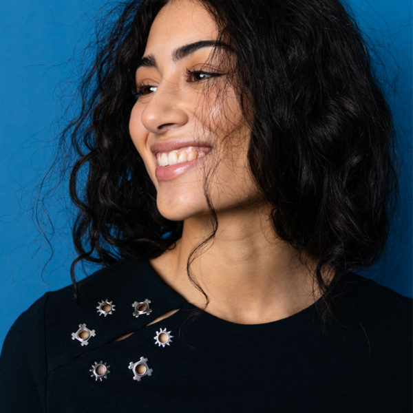 Profil-Aufnahme eines lächelnden Modells mit Blick auf die Ösen-Applikation im Schulterbereich des Shirts von Stitch by Stitch